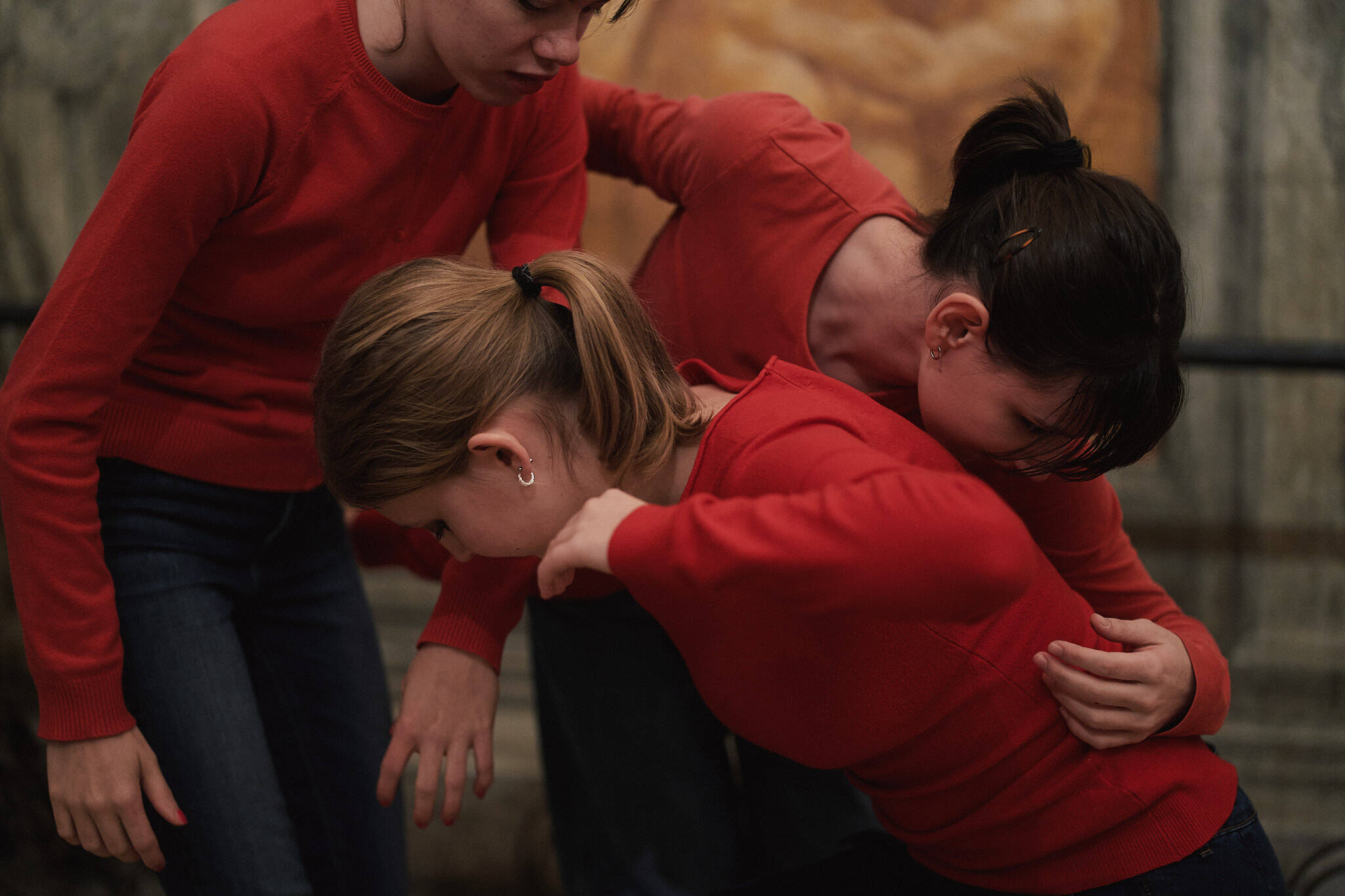 Tre danzatrici adolescenti danzano insieme, quasi abbracciate, in un museo. 